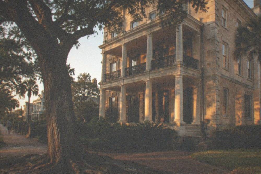 A historic three-story stone mansion with a wide porch in evening light