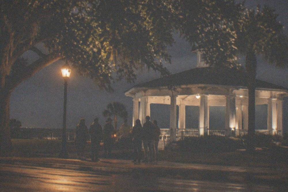 A small group of people gathered around a guide holding a lantern on a sidewalk at night
