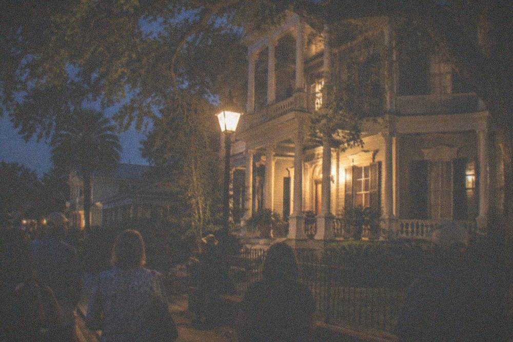A lantern-lit walking tour group paused outside a historic Galveston building