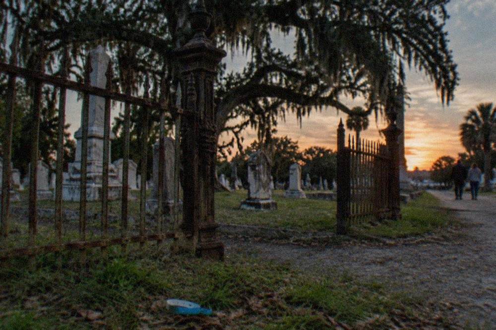 A weathered Galveston cemetery gate with old iron fencing under an evening sky