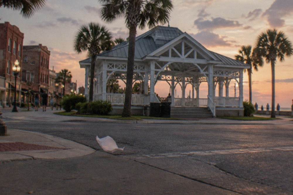 A corner gazebo in a residential historic district at dusk with palm trees and old brick buildings
