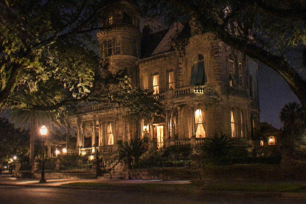 A historic three story Italianate mansion on a tree lined residential street in the evening
