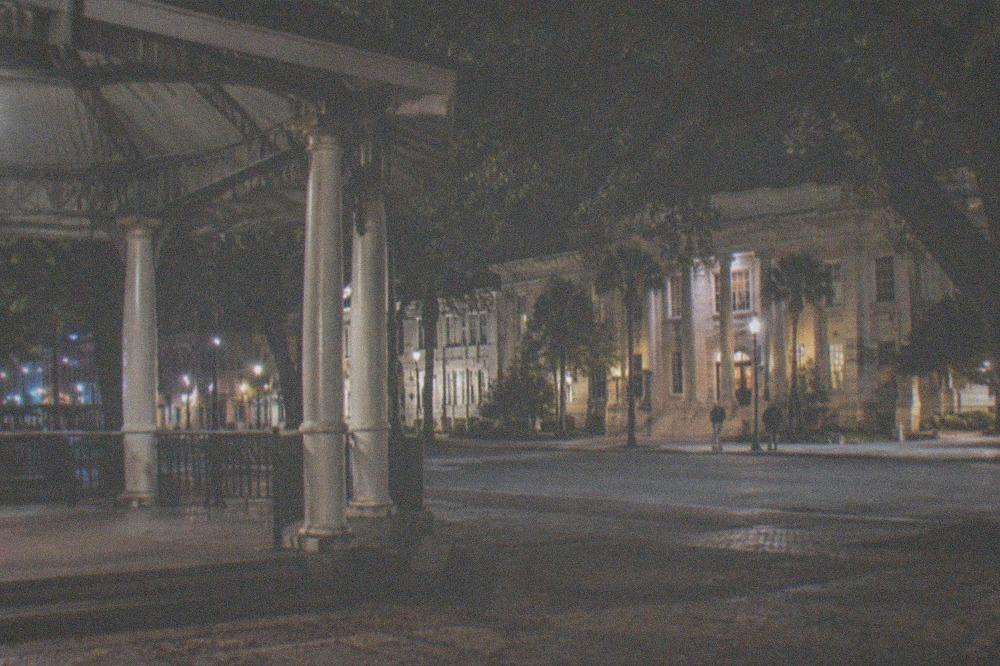 A corner gazebo under streetlights beside a historic library building at night
