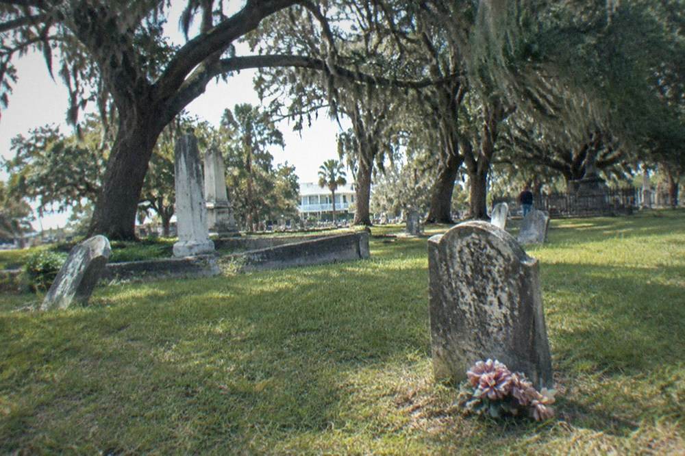 Weathered historic headstones under live oak trees in a Galveston cemetery