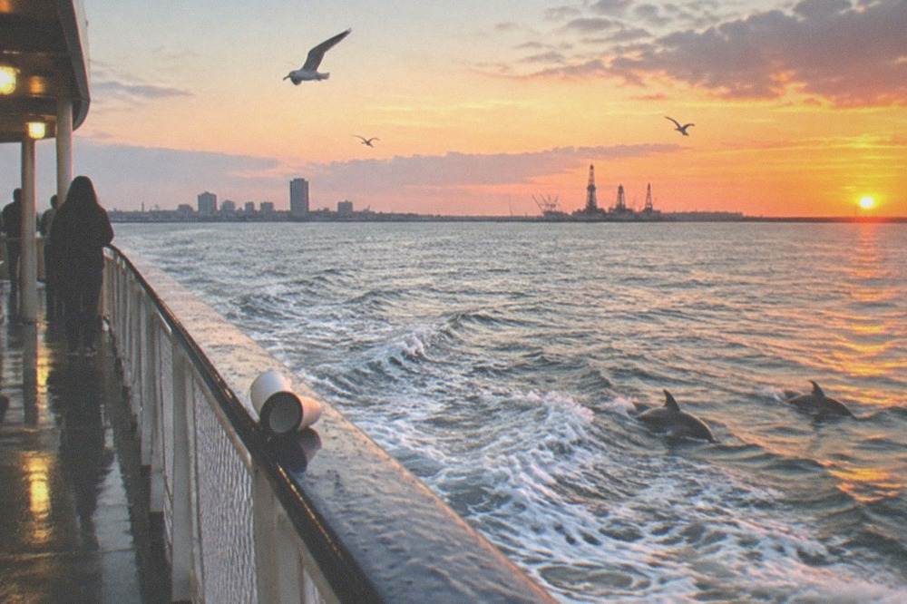 A ferry boat crossing the Galveston ship channel at dusk with gulls overhead