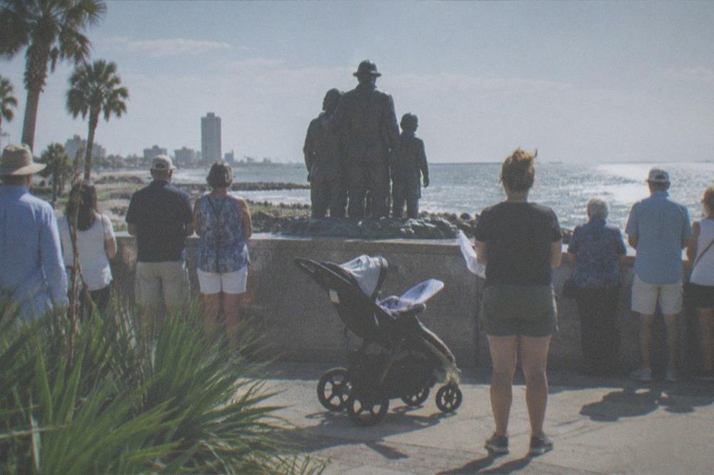 Crowd gathered at a seaside memorial monument on a bright morning
