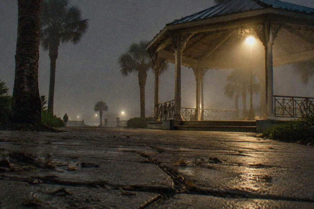 A wooden gazebo on a dark street corner illuminated by a single lamp