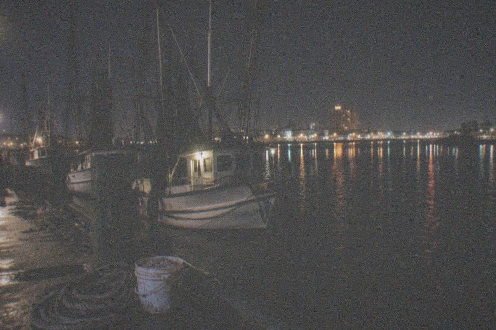 A boat harbor at night with dark water reflecting pier lights and moored vessels