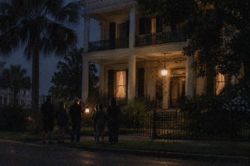 A family of silhouettes standing with a tour guide holding a lantern outside a historic Galveston building at night