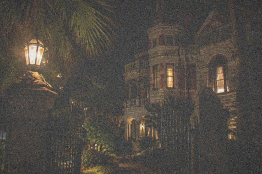 A Victorian mansion facade lit softly at night with palm trees in front