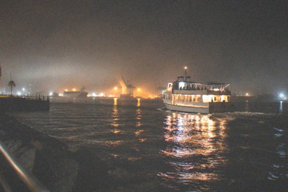 A boat cruising on dark harbor water at night with city lights reflecting on the surface