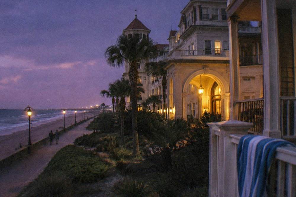 A grand beachfront hotel with a tall arched entryway lit warmly against an evening sky.