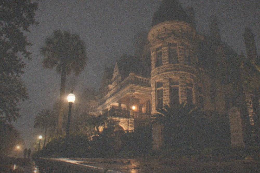 A stone Victorian residence with carved details and a corner turret glowing under streetlights.
