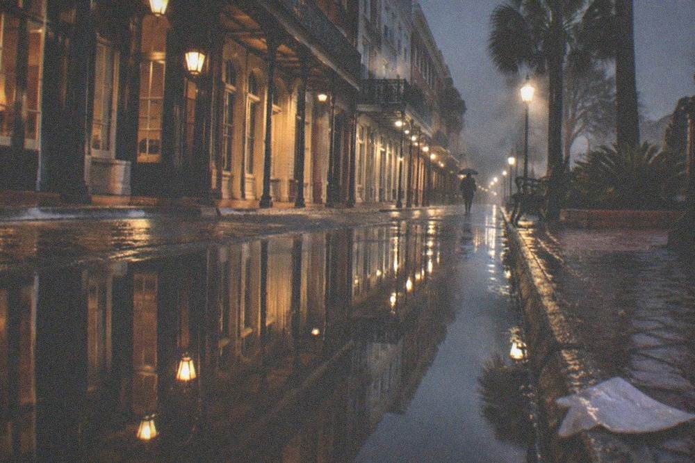 A rain-wet Strand sidewalk reflecting the lights of closed storefronts at night